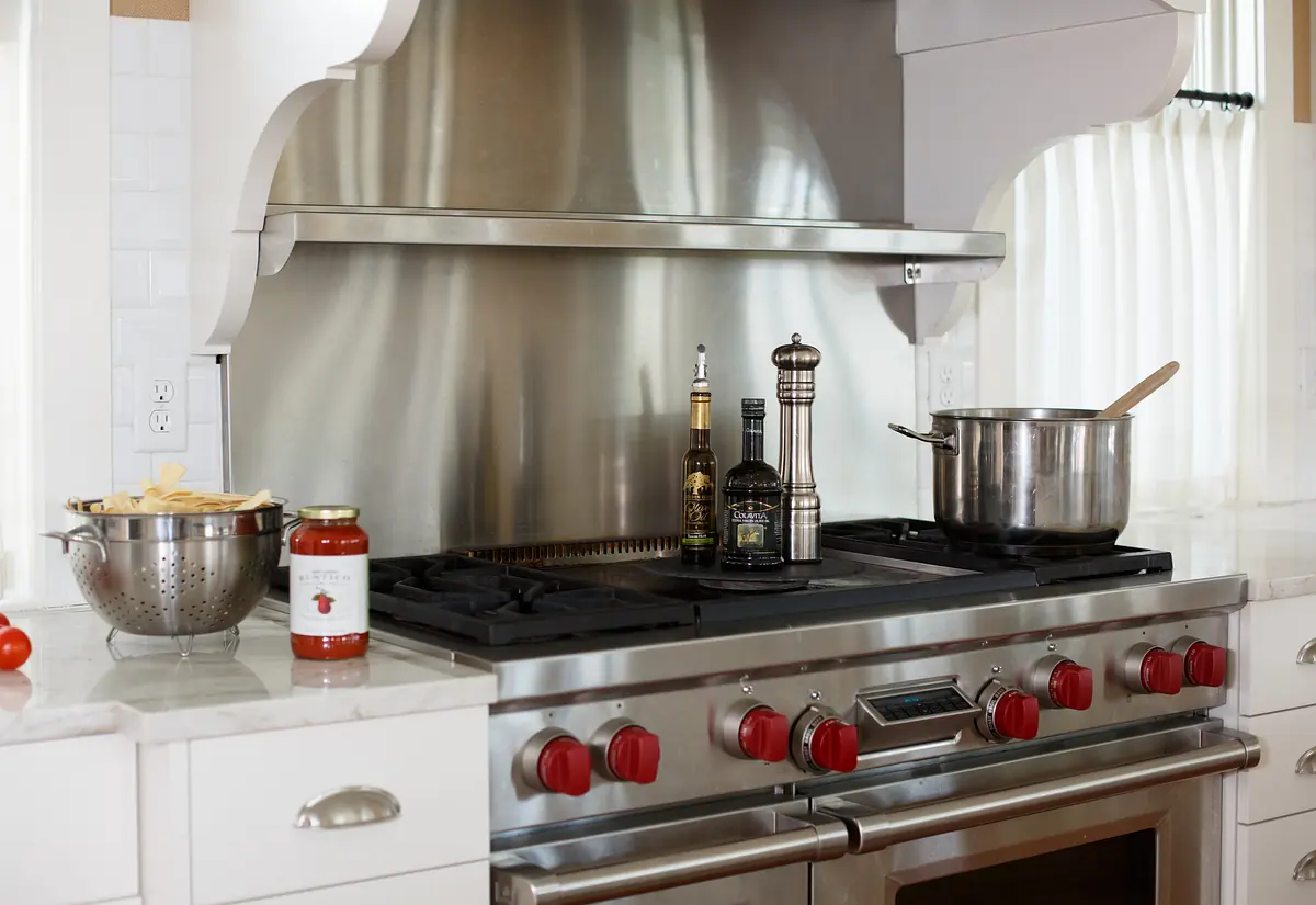 Kitchen with stainless steel gas range, marble countertop, decorative hood, and various cookware.