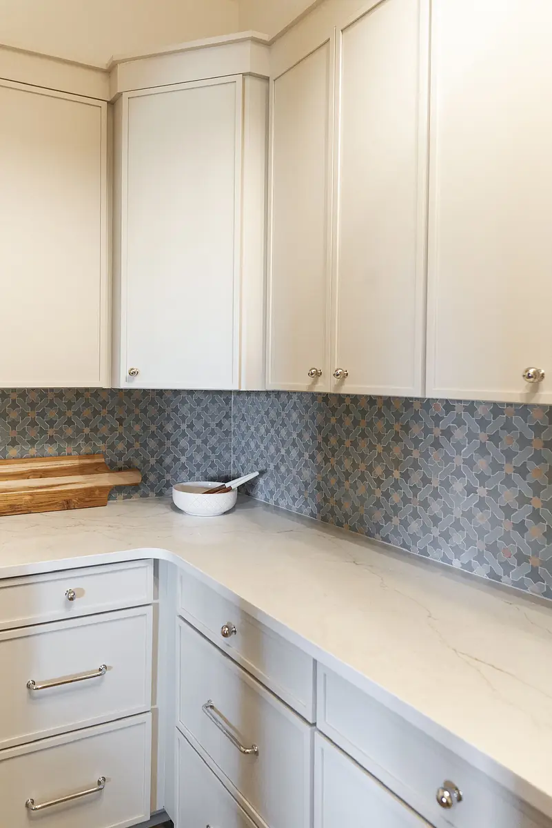 Kitchen with white cabinetry, light countertop, decorative tiled backsplash, cutting board, and white bowl.