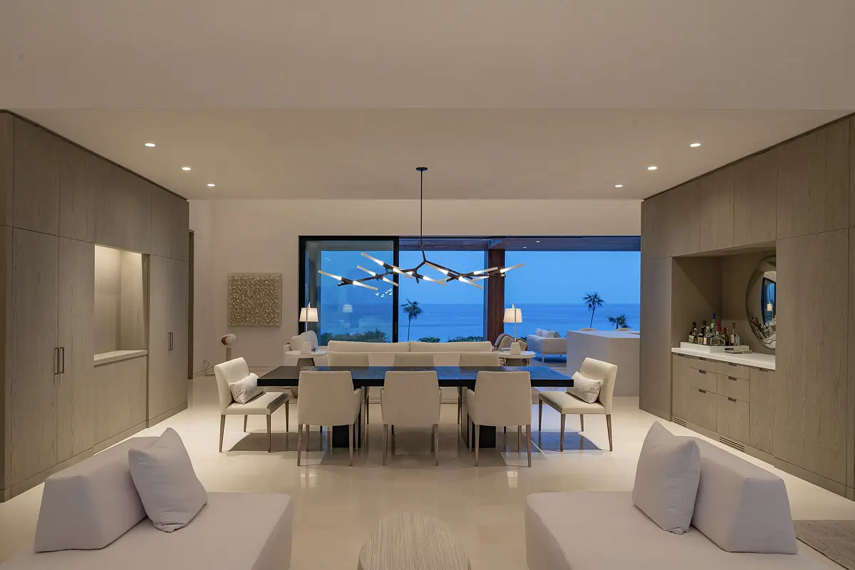 Dining room with long table, white chairs, ocean views, built-in storage, and modern chandelier