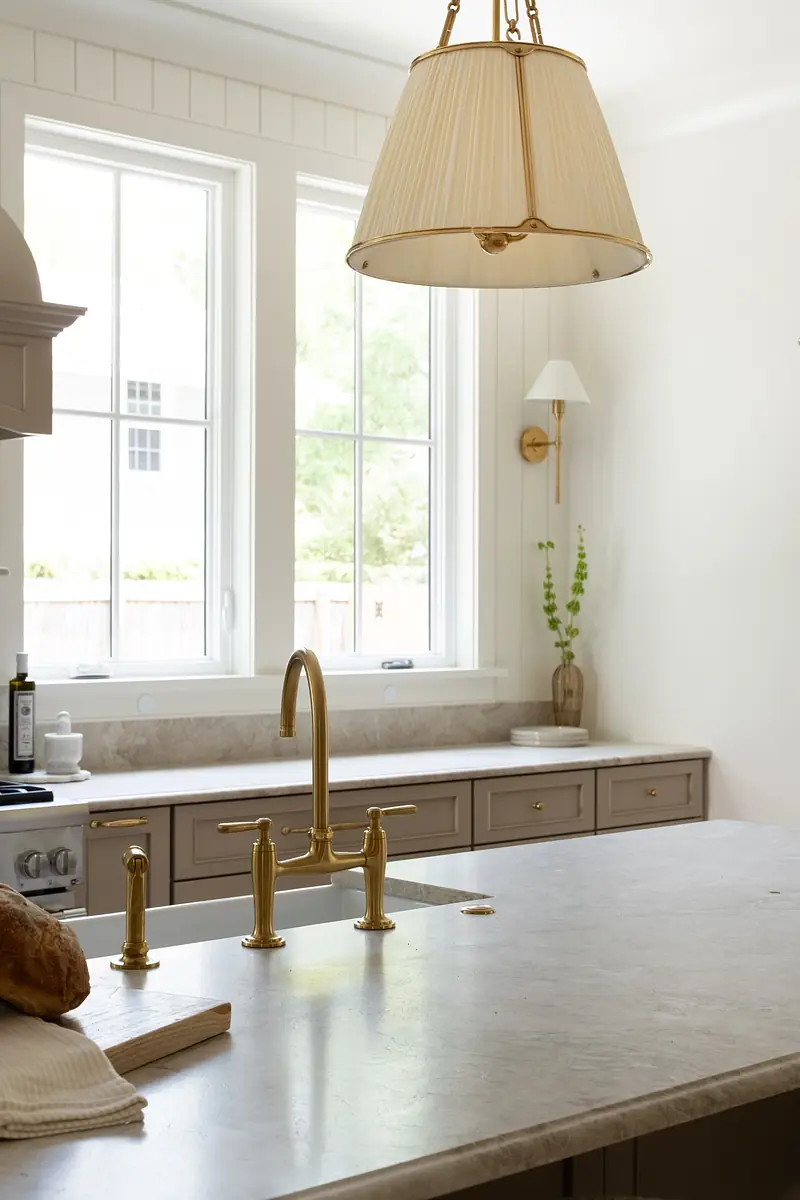 Kitchen with central island, stone countertop, brass faucet, cabinetry, and natural light from large windows