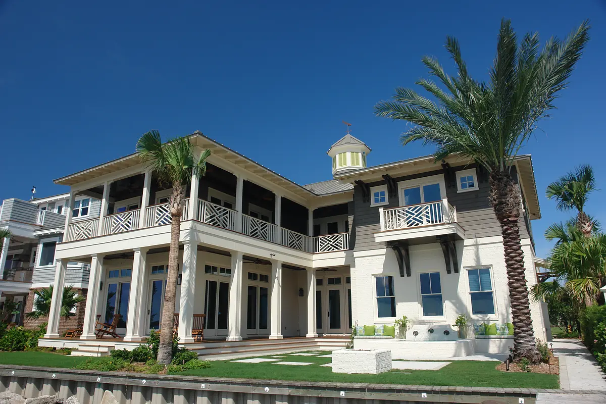 Exterior front of a two-story house with light siding, dark wood accents, palm trees, and a balcony.