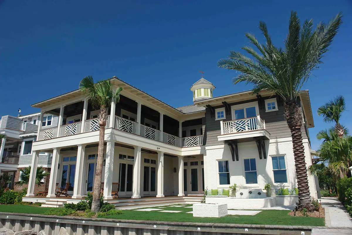 Coastal-style house with two stories, front porch, large windows, and palm trees.