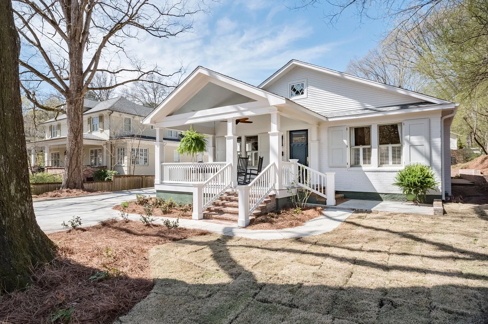 Front exterior view of a white house with a porch, driveway, and surrounding landscaping.