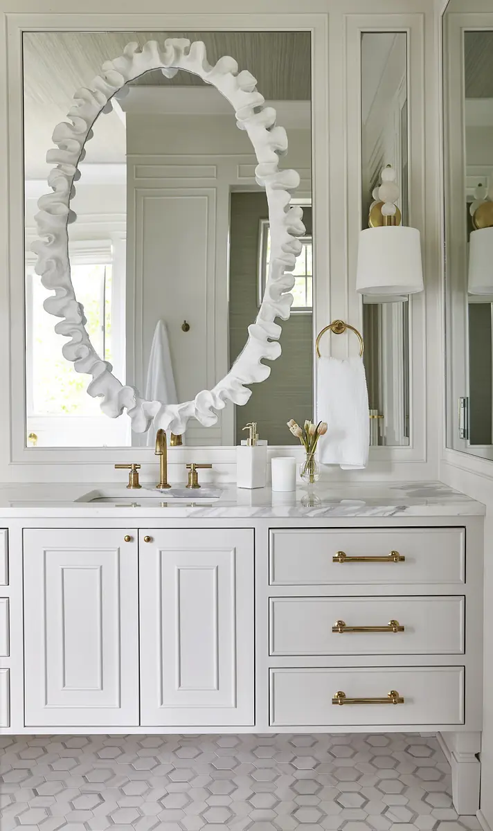 Bathroom with double sink vanity, gold fixtures, large oval mirror, and hexagonal tile floor.