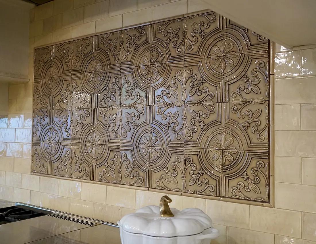 Kitchen backsplash with intricate relief tiles and a white ceramic container on the countertop.