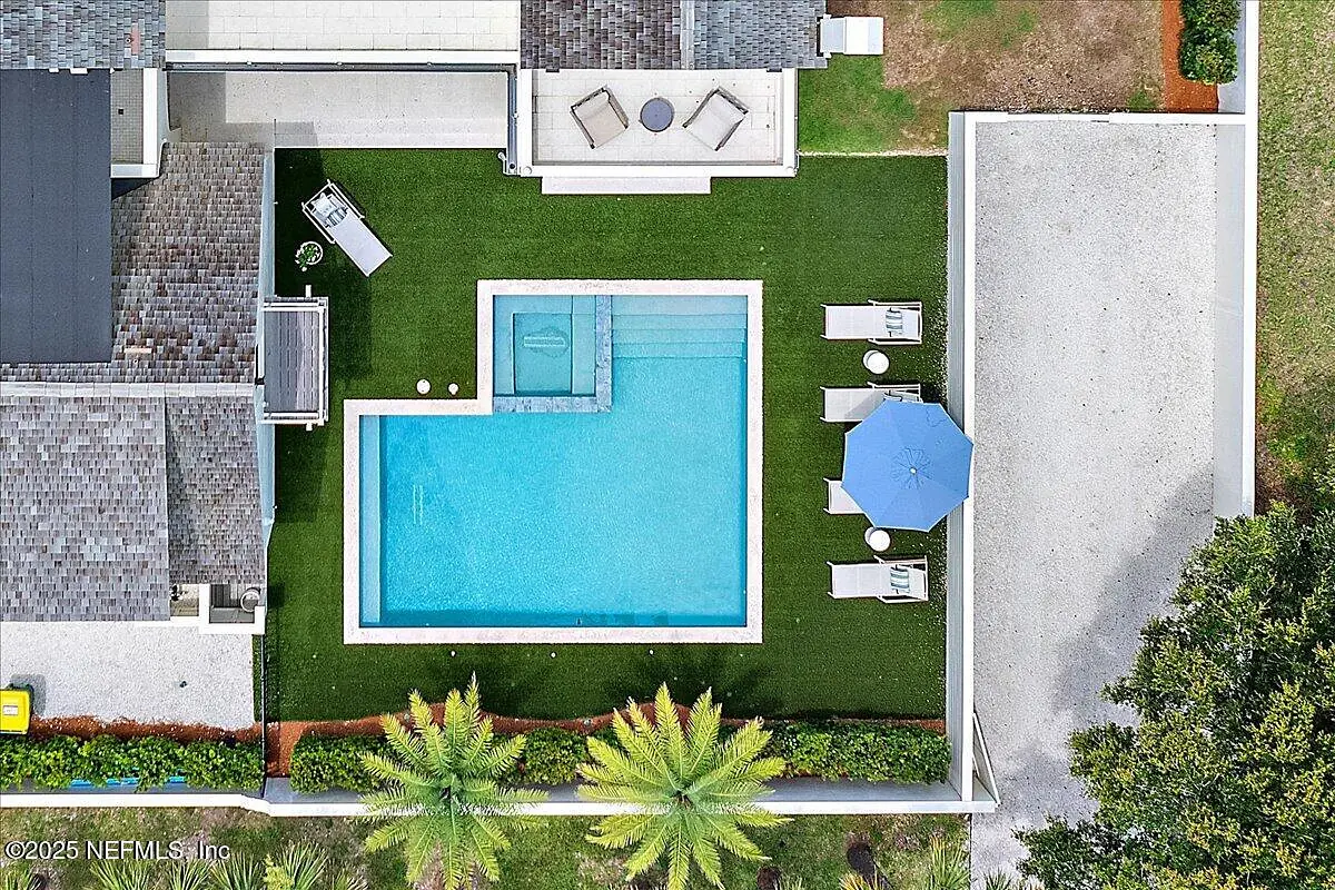 Outdoor patio with swimming pool, lounge chairs, dining table, and landscaped grass.