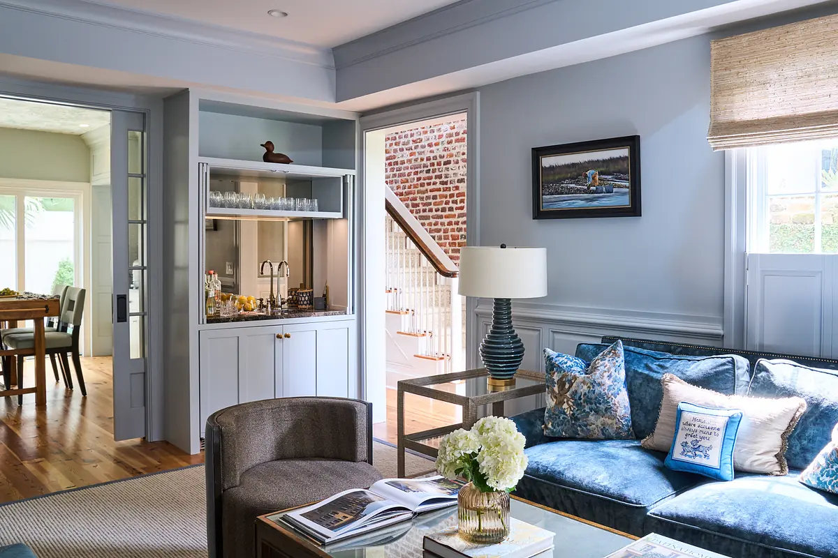 Living room with blue velvet sofa, coffee table, glass-front cabinet, and framed painting.