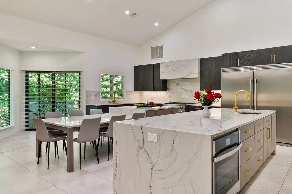 Kitchen with marble island, stainless steel appliances, dark cabinetry, dining table, and natural light from windows