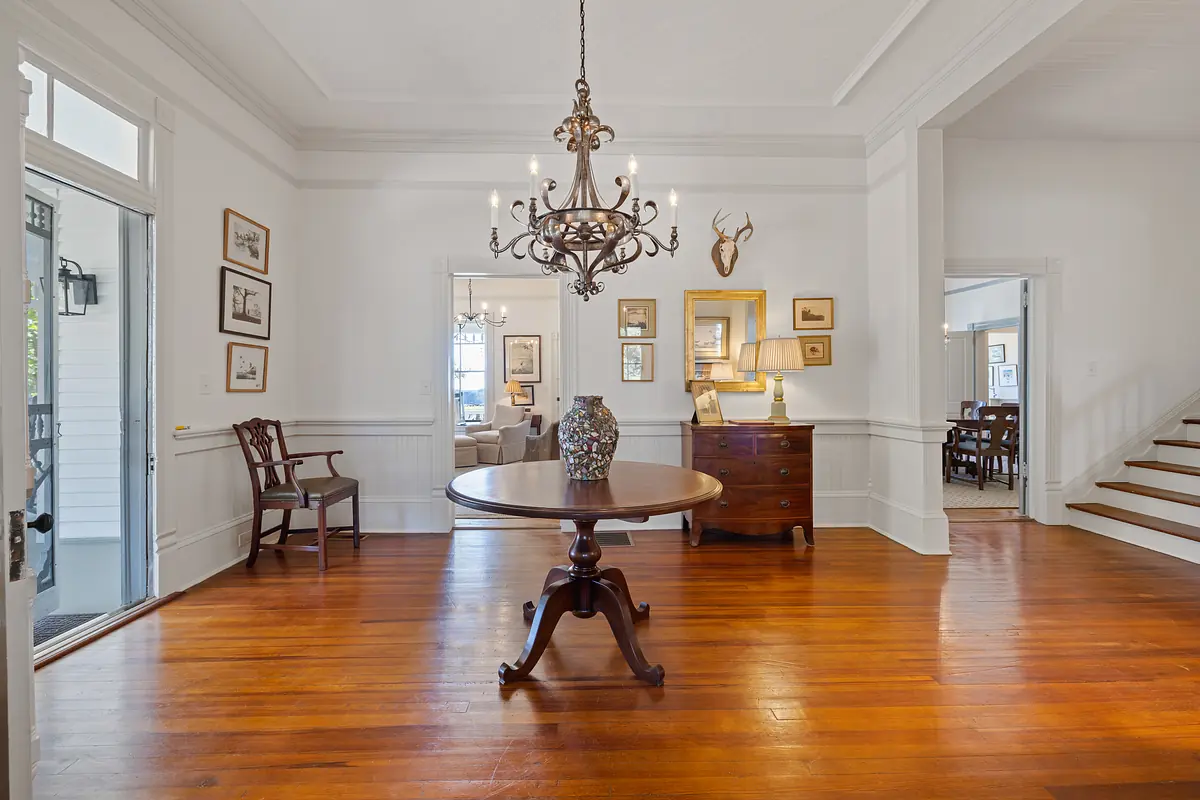 Foyer with round table, vase, chair, sideboard, artwork, chandelier, and staircase.