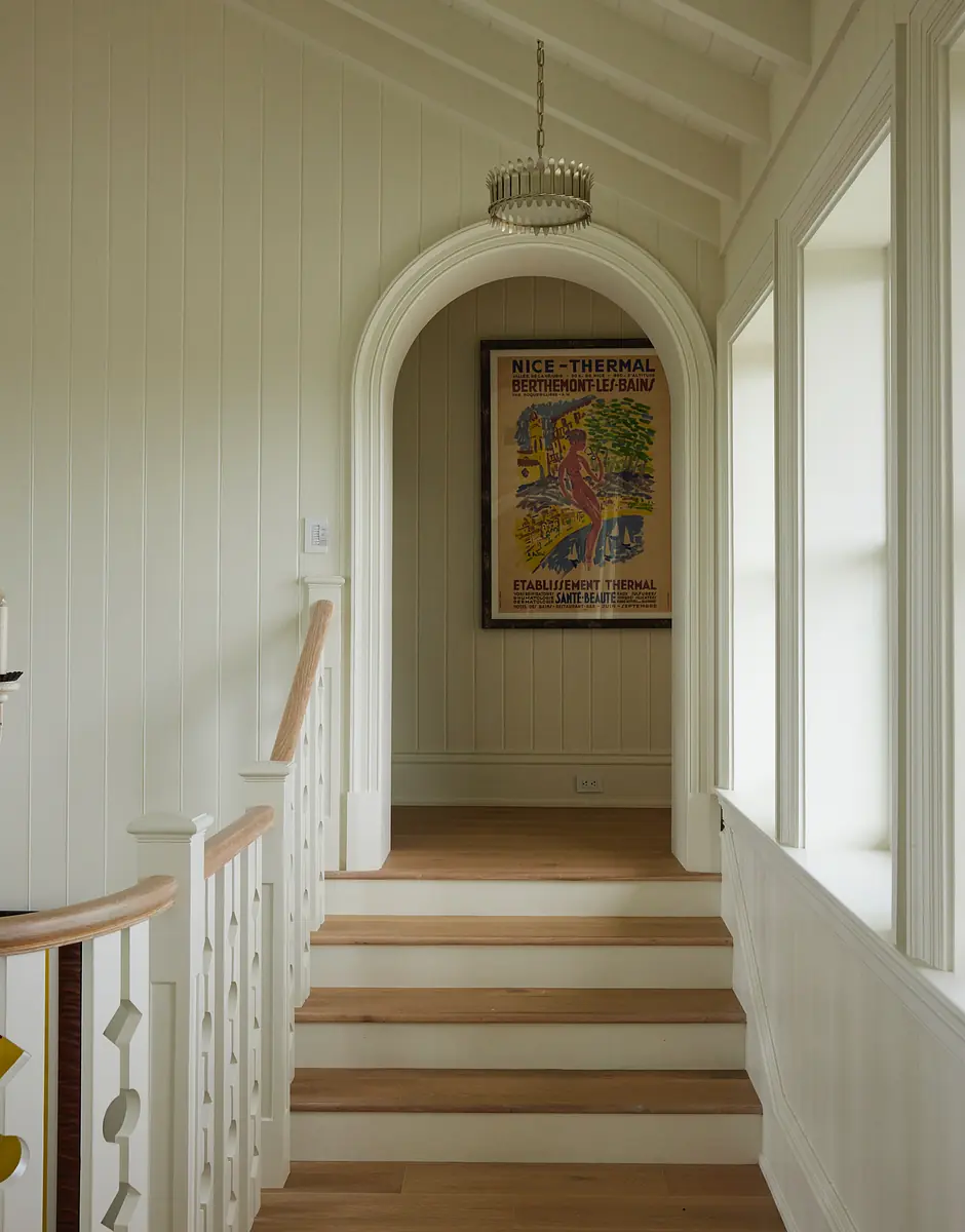 Hallway with wooden staircase, arched doorway, vintage poster, and decorative chandelier