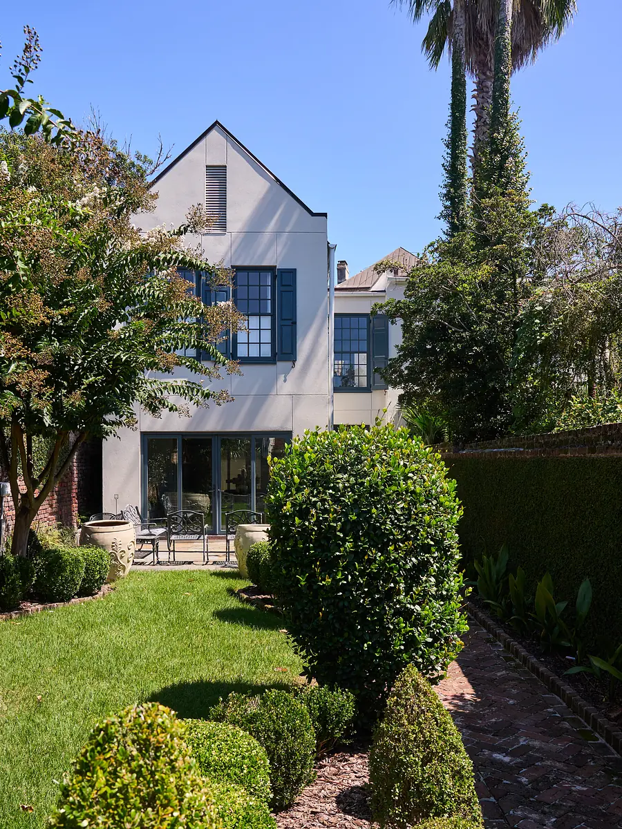 Garden with manicured lawn, trimmed hedges, potted plants, and seating area with table and chairs.