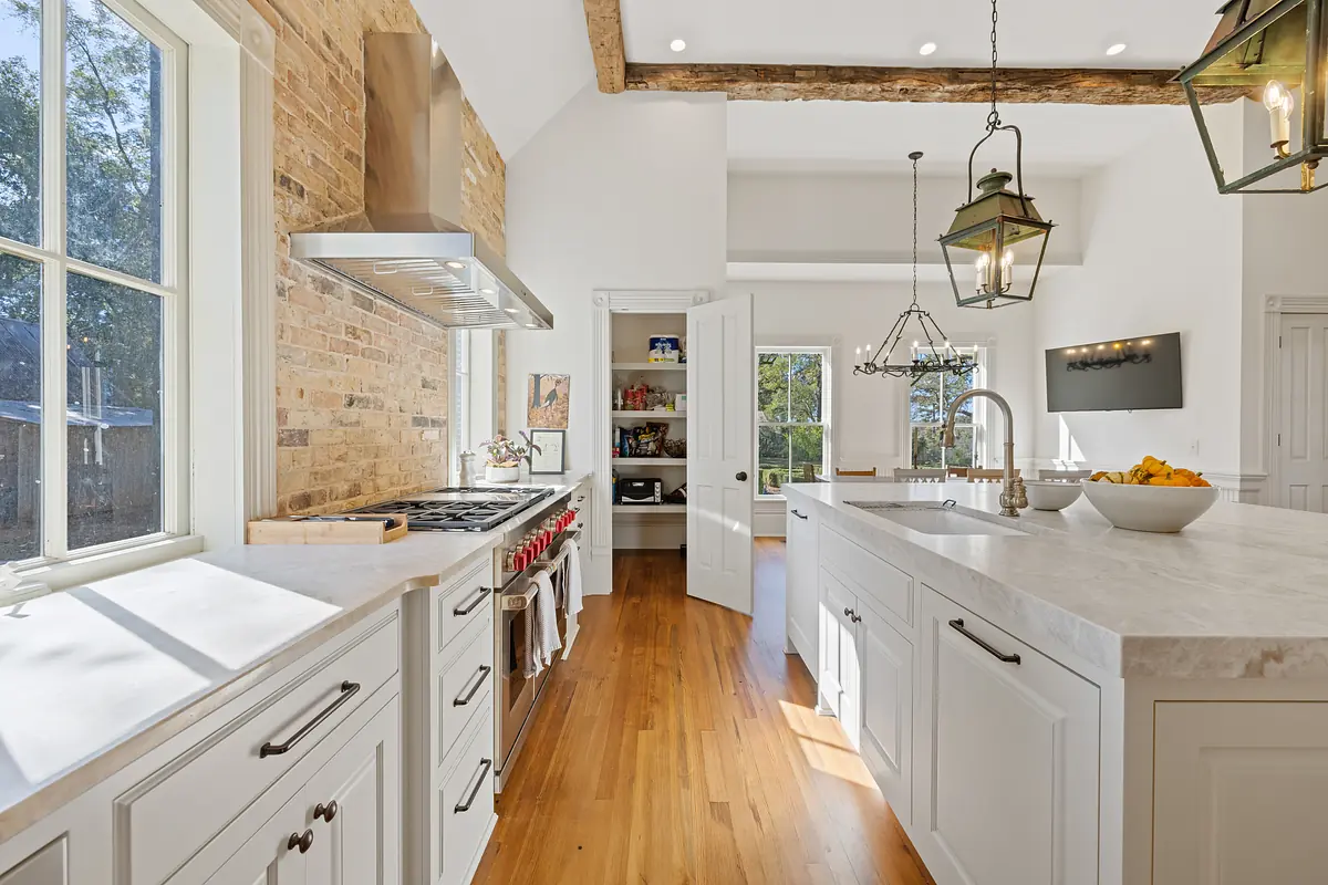Kitchen with marble island, gas stove, wood cabinets, exposed beams, and pendant lights.