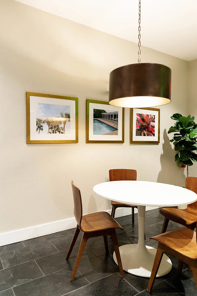Dining room with round white table, four wooden chairs, three framed pictures, and a potted plant.