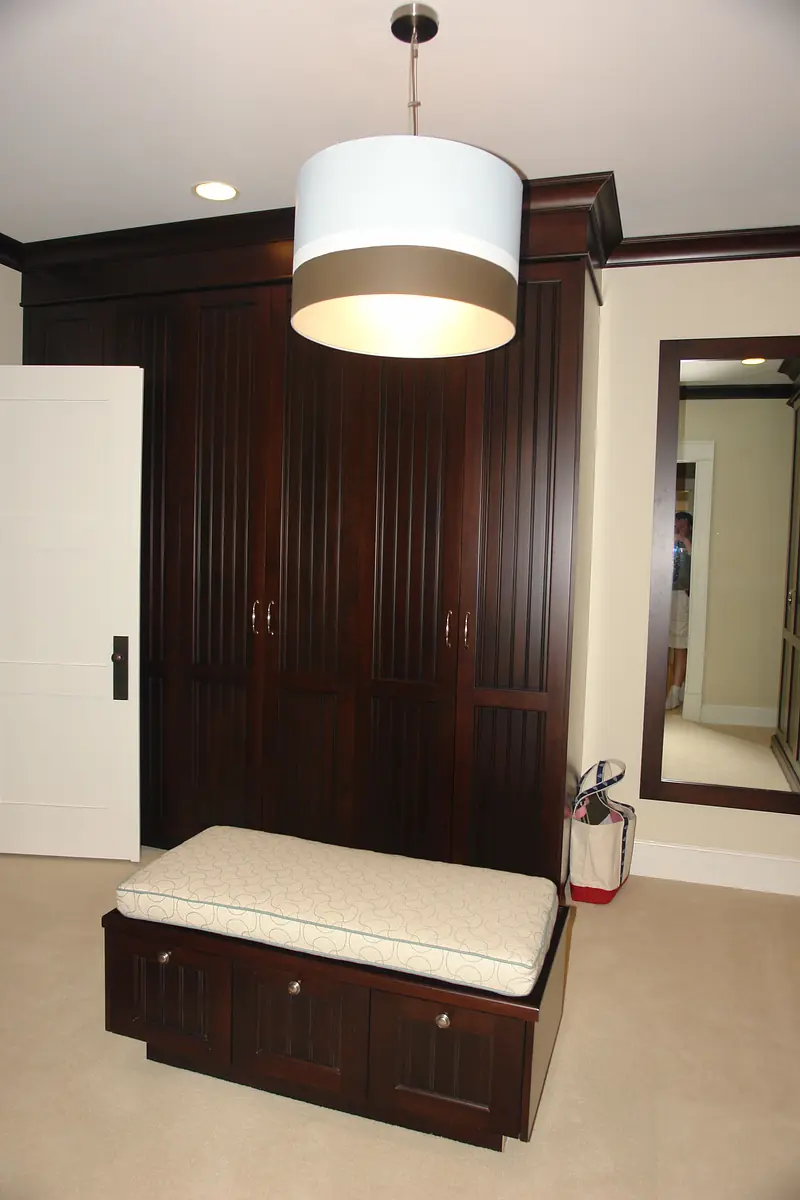 Mudroom with dark wooden storage, white bench, large mirror, and light-colored carpet