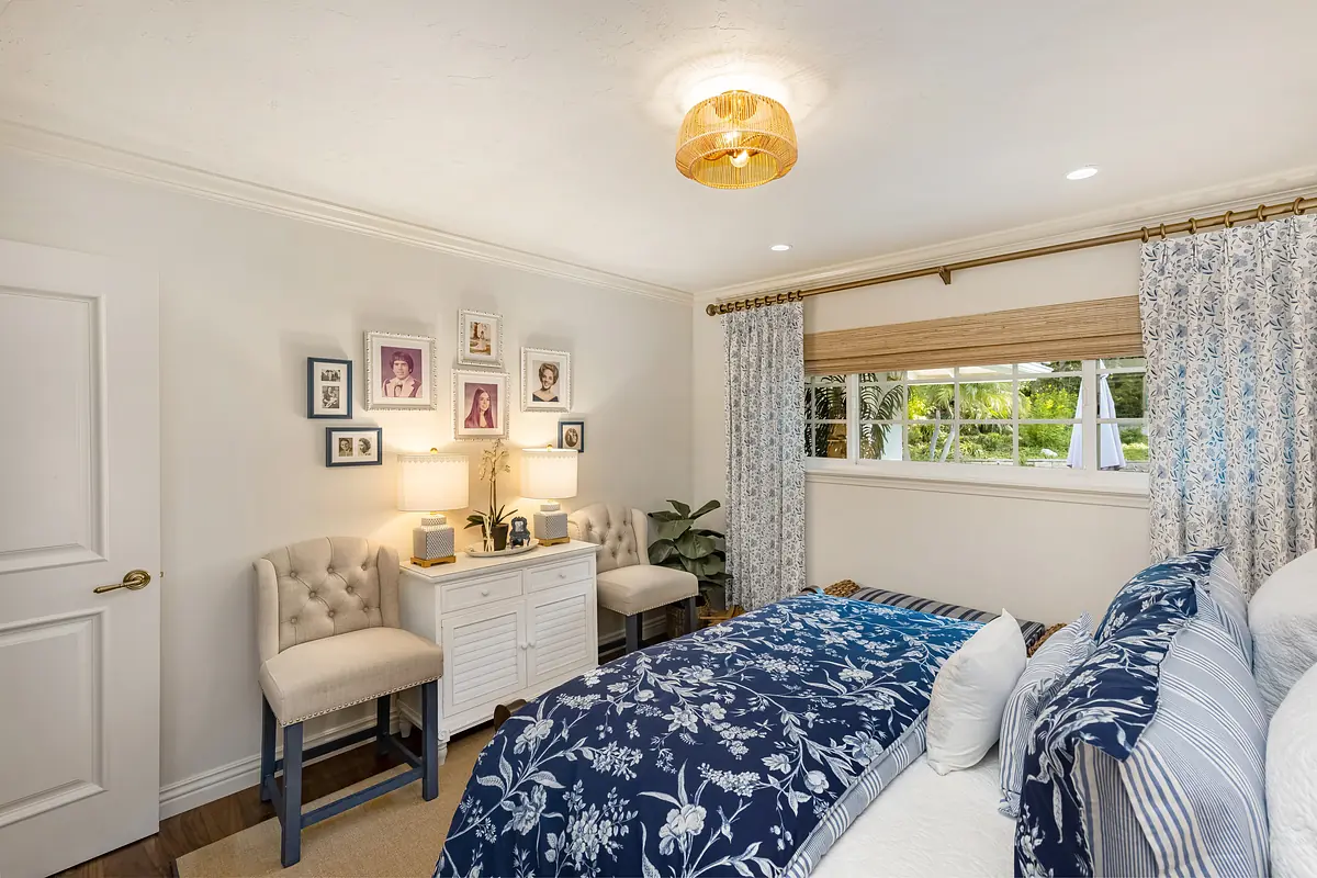 Bedroom with bed, tufted chairs, white dresser, lamps, and framed pictures on the wall.