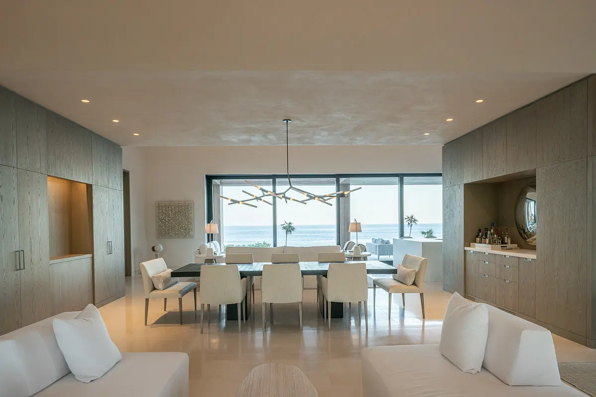 Dining room with rectangular table, white chairs, ocean views, built-in cabinet, and contemporary chandelier.