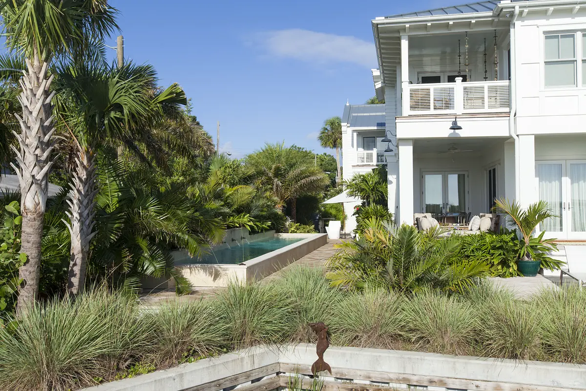 Exterior rear view with a pool, tropical plants, patio area, and second-story balcony.