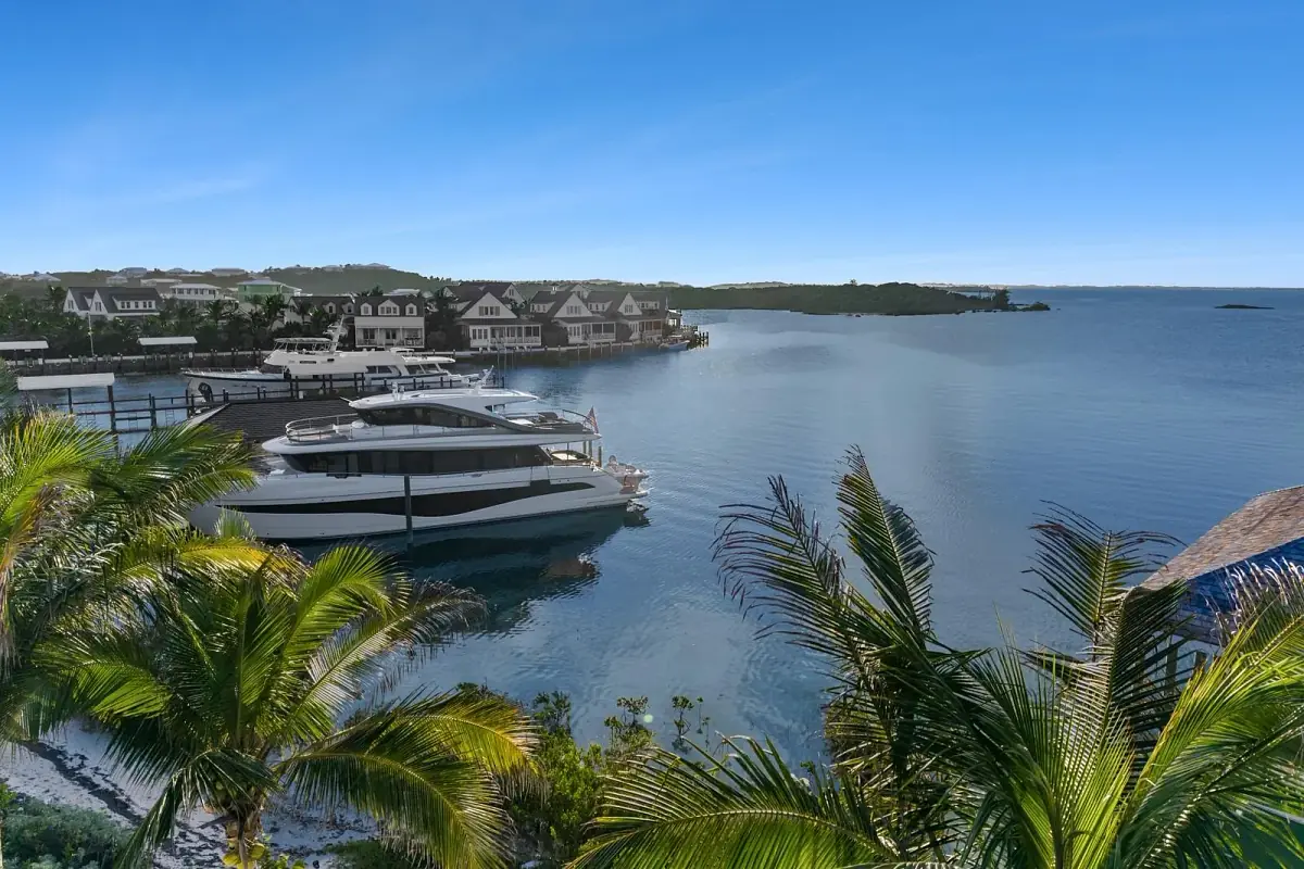 Waterfront view with marina, boats, houses, greenery, and blue sky.