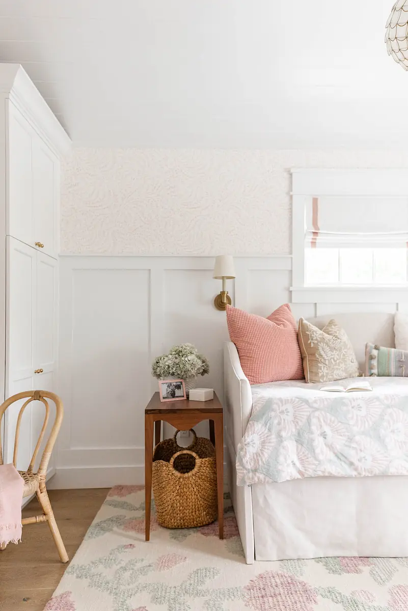 Bedroom with daybed, nightstand, photographs, basket, and patterned rug against paneled walls.