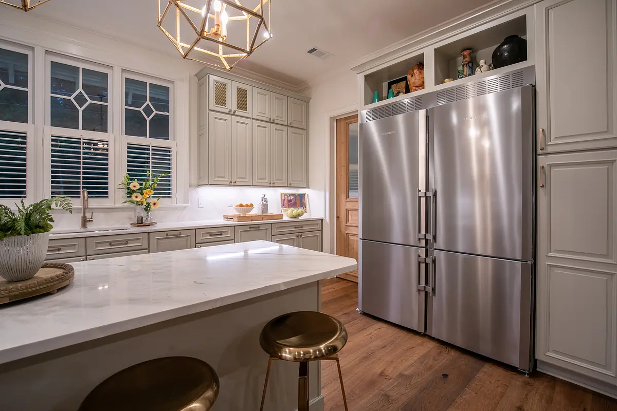 Kitchen with stainless steel refrigerator, white cabinetry, marble countertop, and gold bar stools.