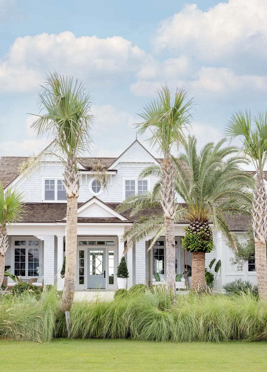 Front exterior of house with palm trees, grass, shrubs, and large glass doors.