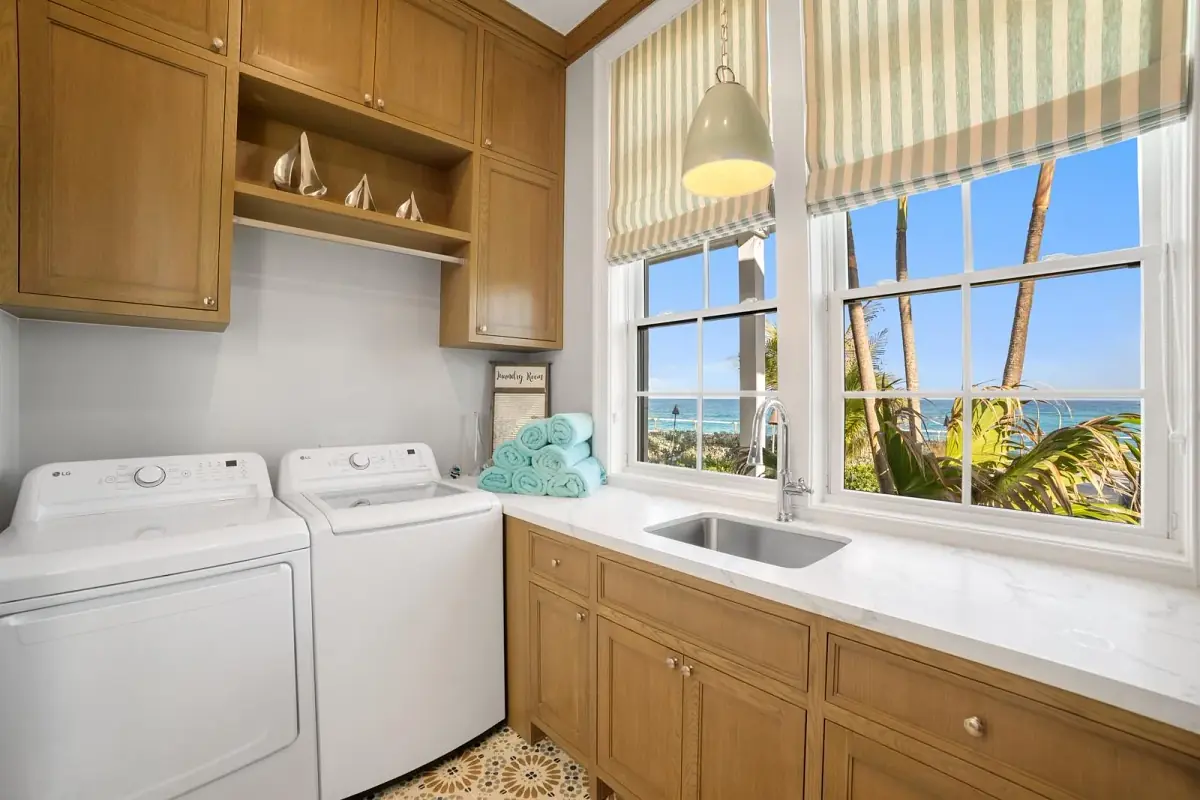 Laundry room with two washing machines, sink, wooden cabinetry, and large windows with striped shades