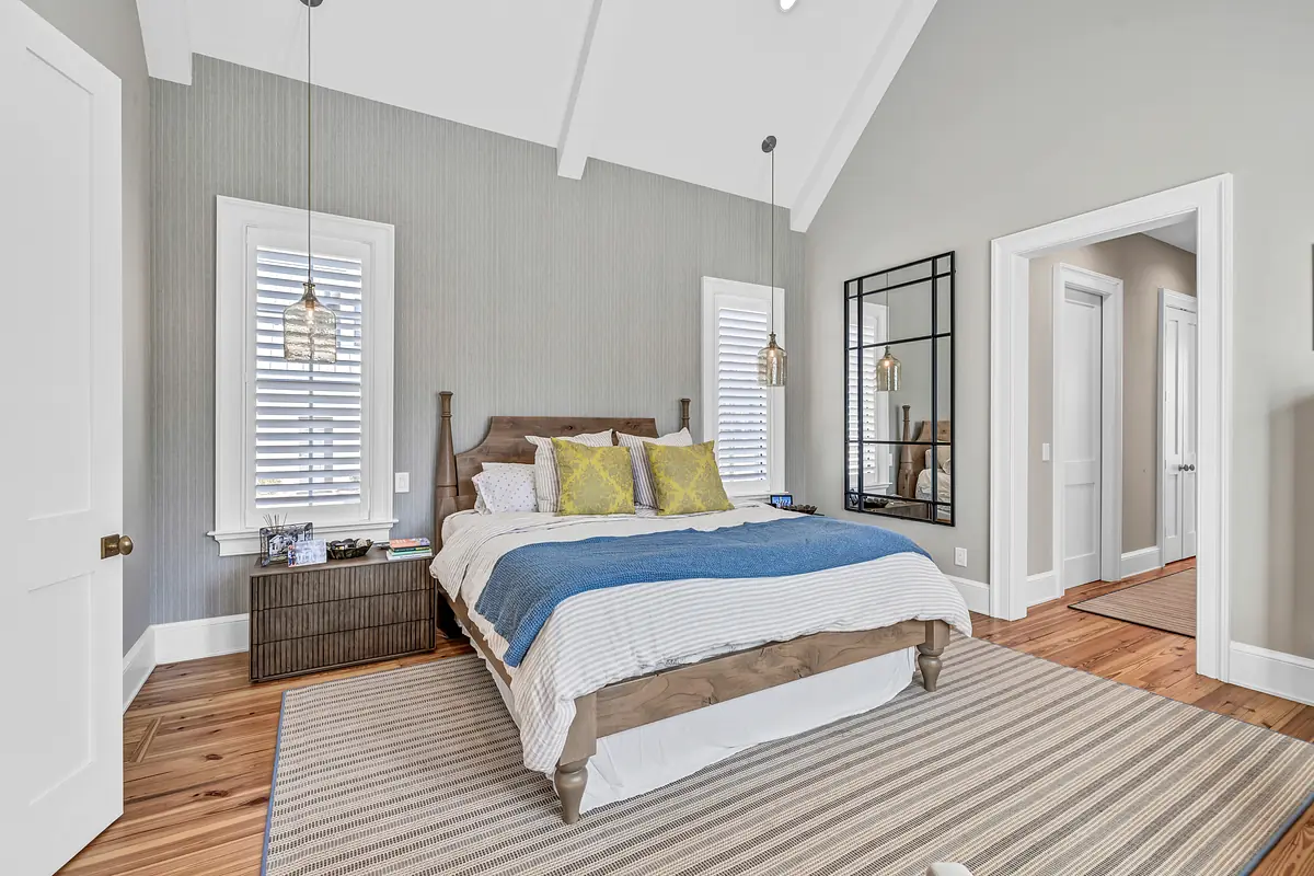 Bedroom with wooden bed, blue blanket, yellow cushions, nightstands, mirror, and gray accent wall.