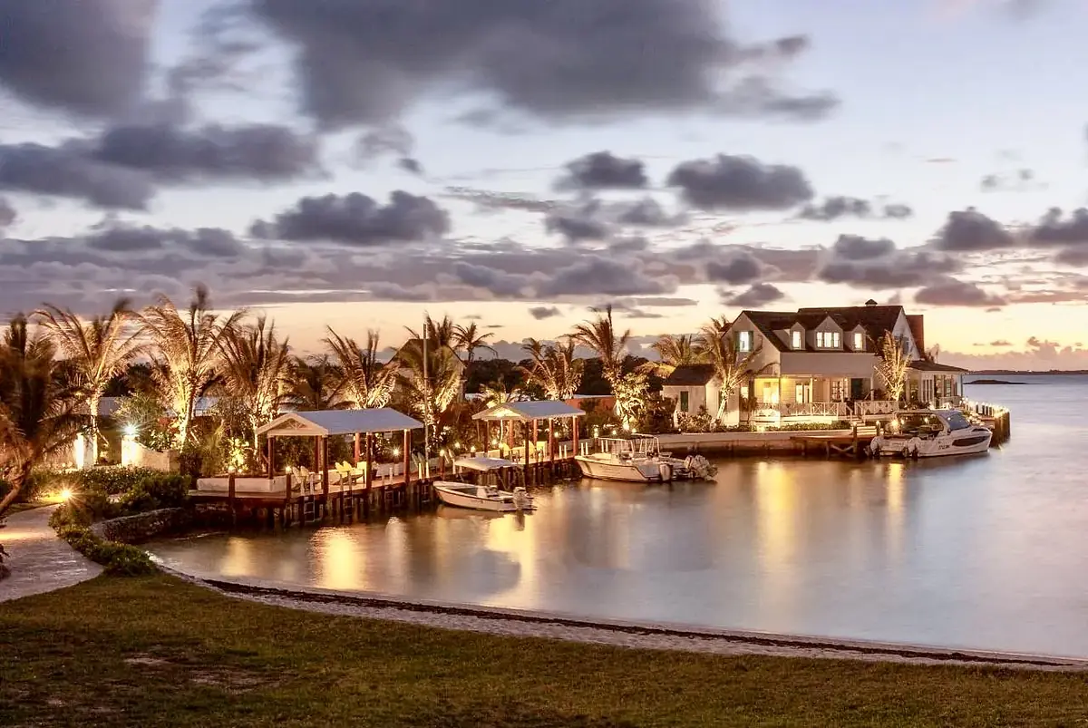 Waterfront property with docks, palm trees, boats, and house visible at twilight with reflections on the water.