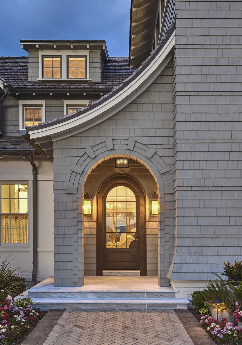 Exterior front view with arched entryway, dark wooden door, wall sconces, and gray shingle façade.
