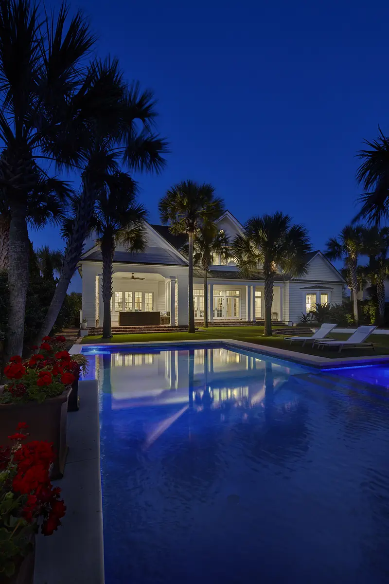 Exterior view with swimming pool, palm trees, planters, lounge chairs, and a house with large windows.