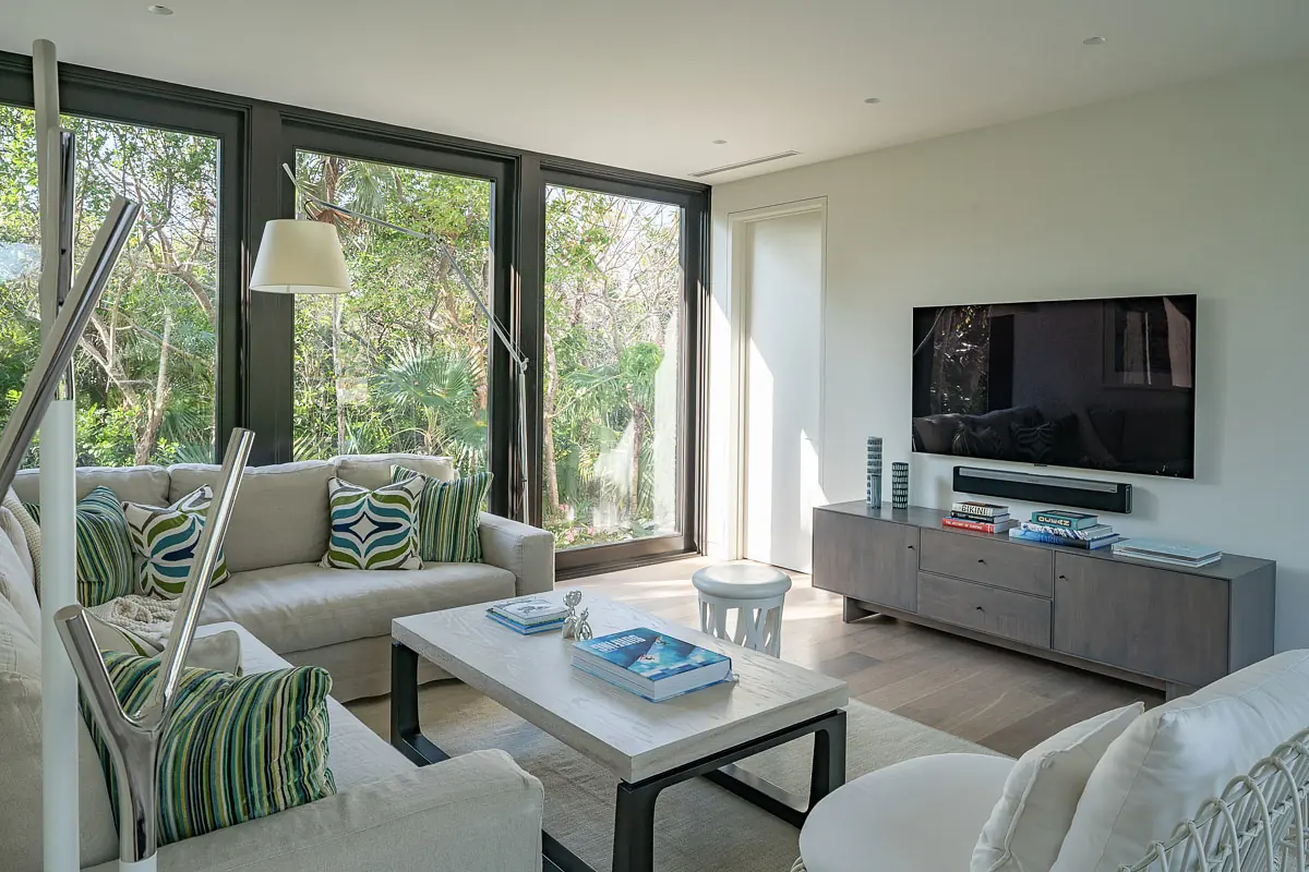 Living room with beige sofa, coffee table, media console, and large windows providing outdoor views