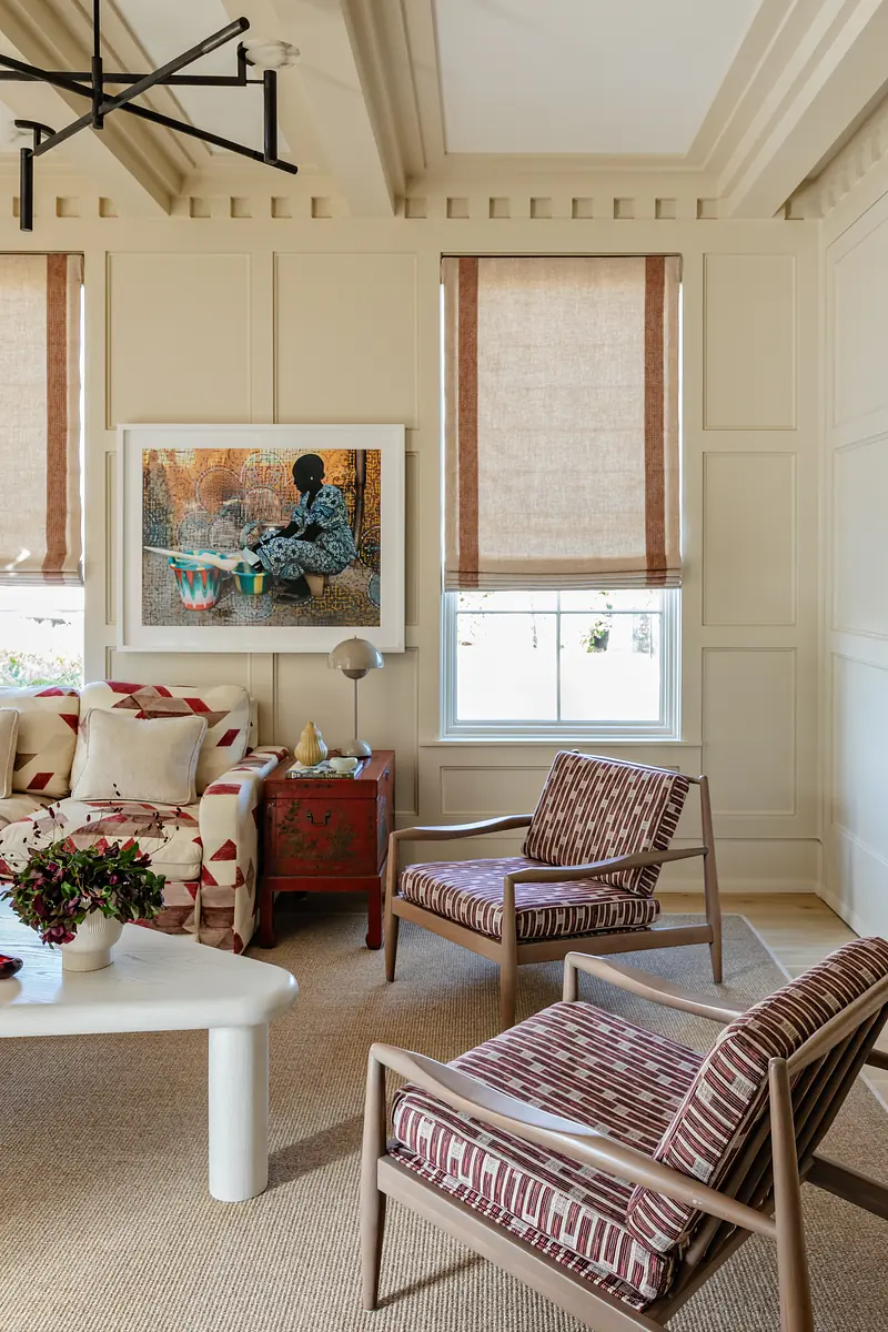 Living room with patterned sofa, striped chairs, white coffee table, and artwork on paneled walls.