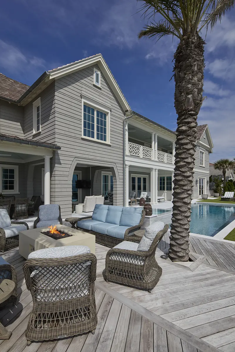 Patio with wicker seating, fire pit table, pool, palm trees, and wooden deck.