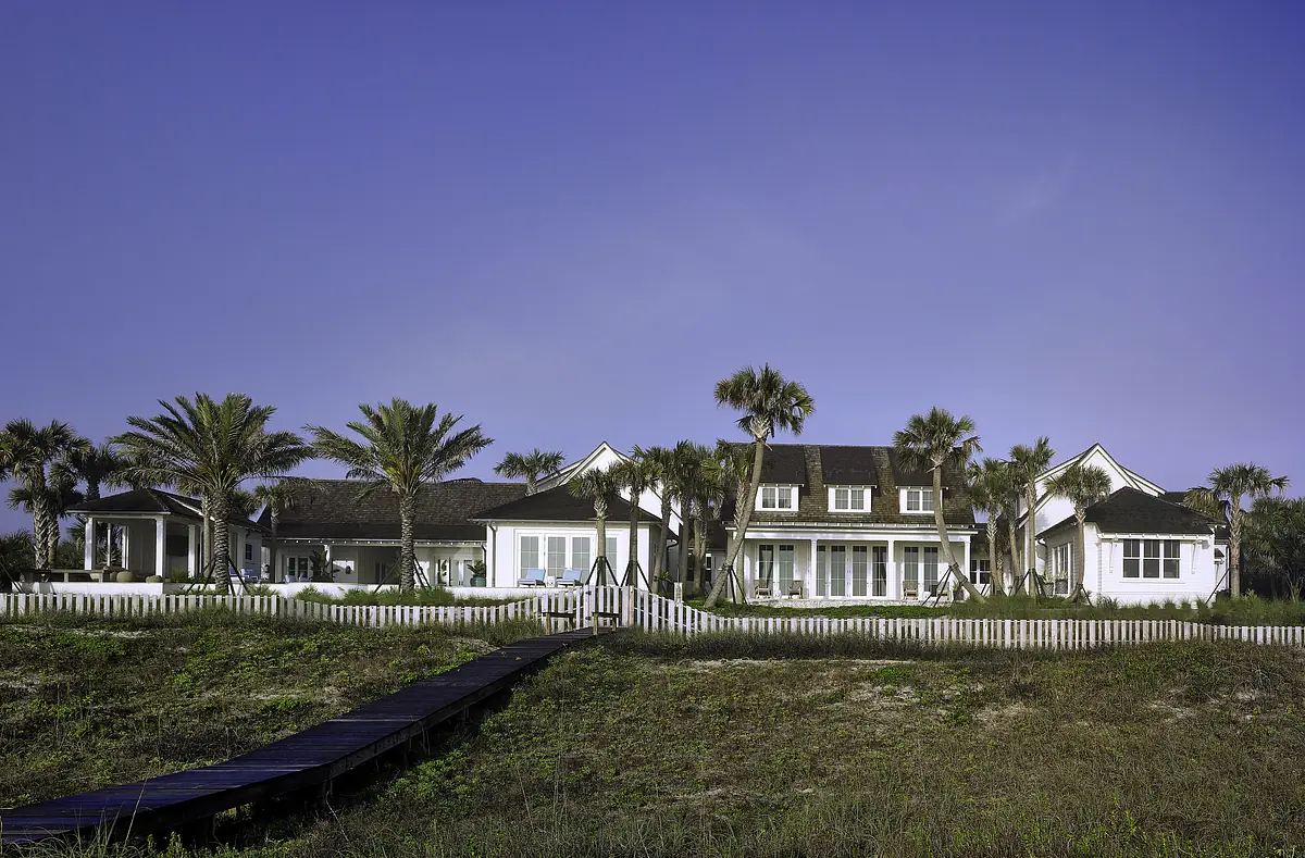Front exterior view of a house with large windows, porch, and palm trees.