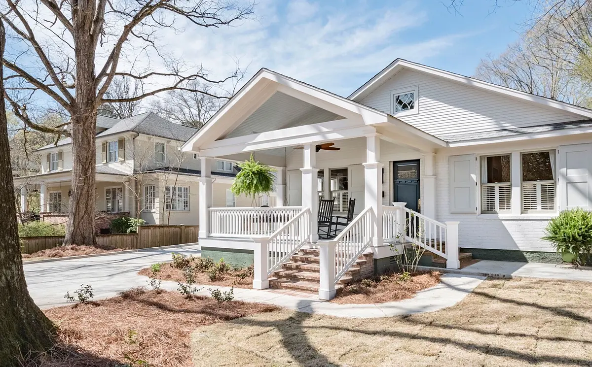Front exterior view of a house with white facade, wooden porch, and landscaping.