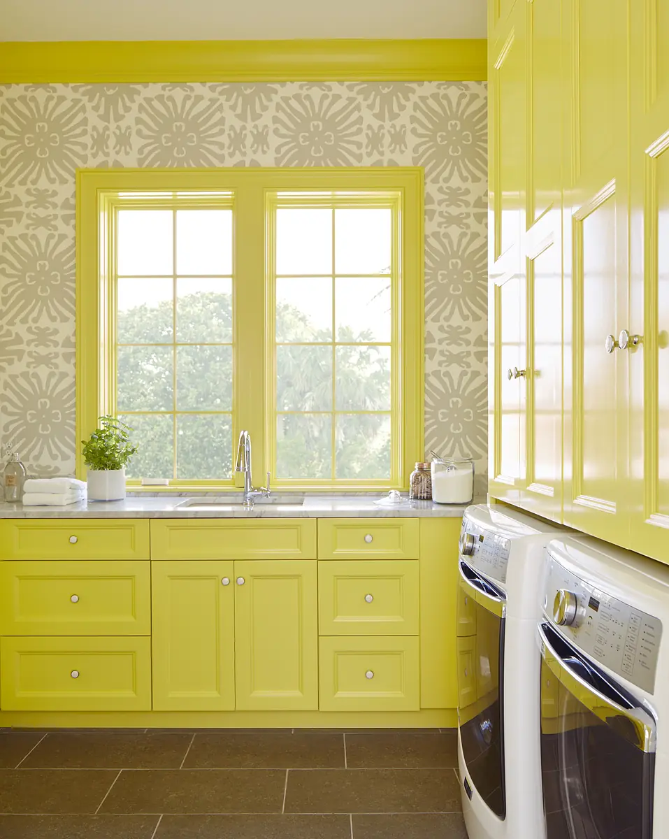 Laundry room with yellow cabinetry, stainless steel sink, white appliances, and floral wallpaper with natural light.