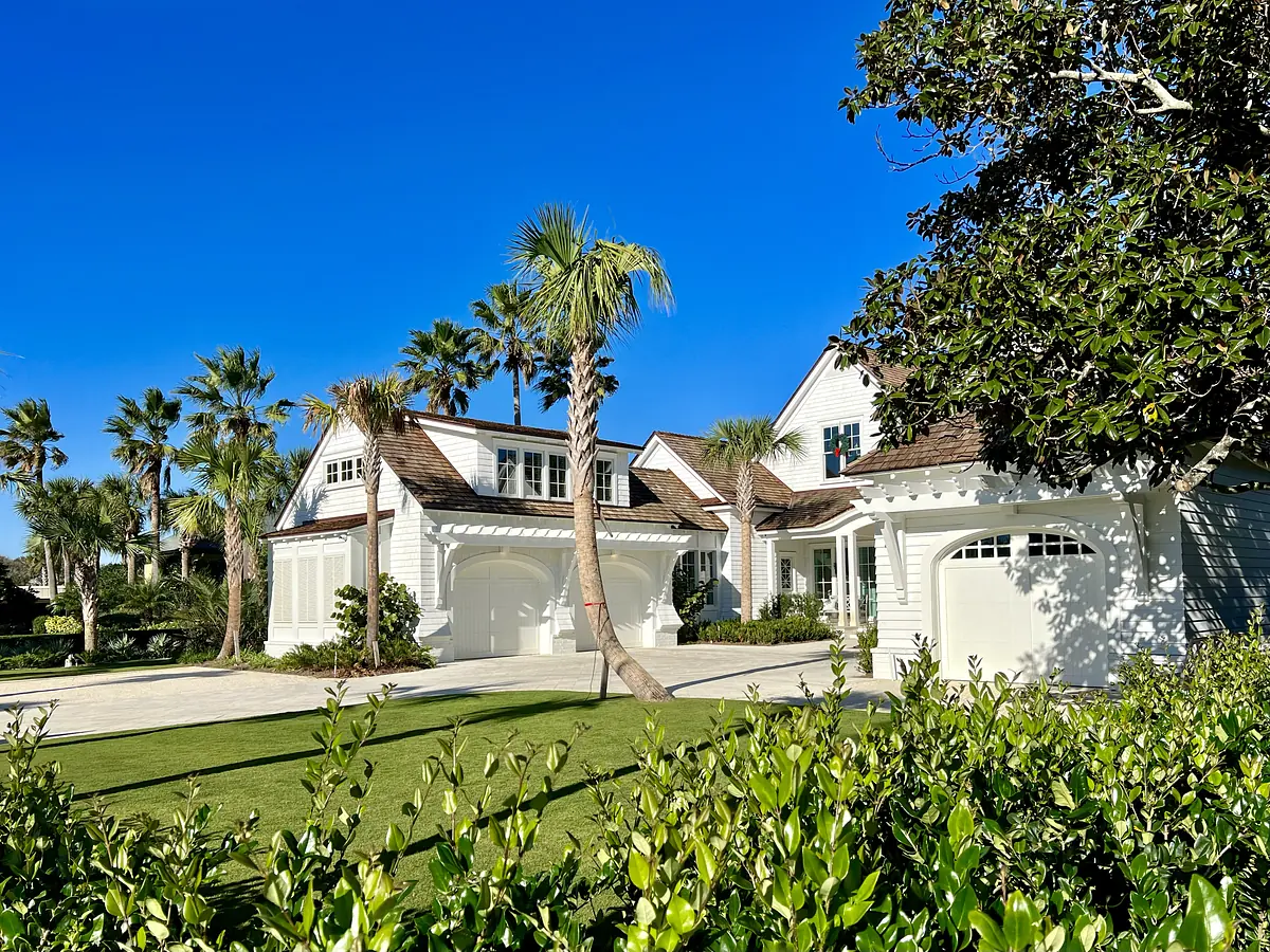 Exterior view of a house with white siding, shingle roof, palm trees, and paved driveway.