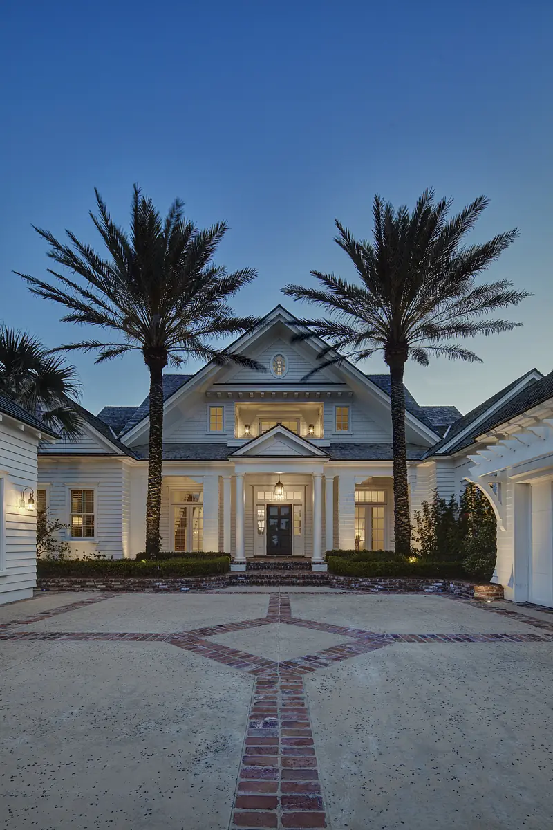 Exterior front of a two-story house with columns, palm trees, brick pathway, and white trim.