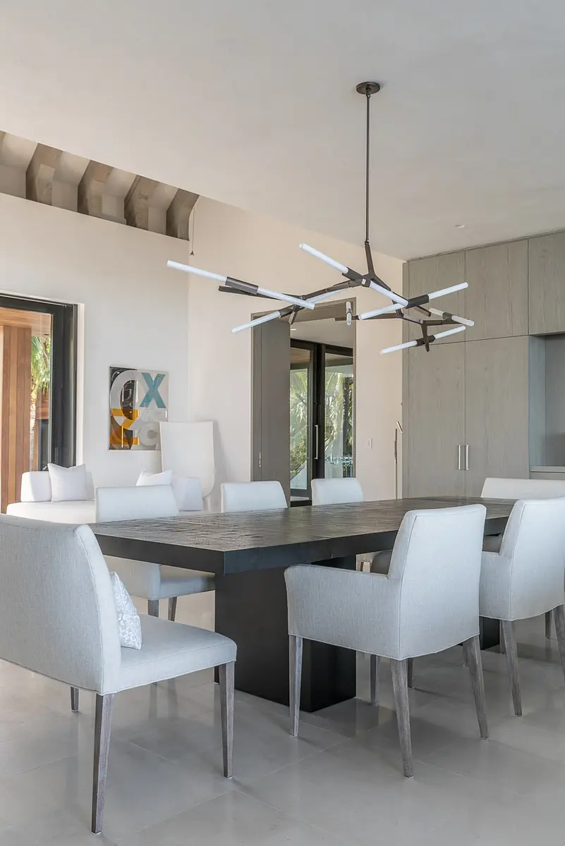Dining room with wood table, upholstered chairs, large window, storage cabinets, and modern chandelier.