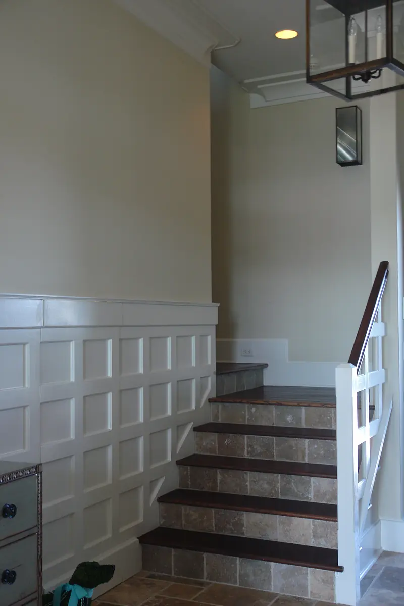 Foyer with staircase, white paneled wall, ceiling lantern, and tile flooring.