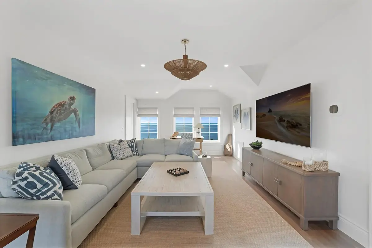 Living room with gray sectional sofa, wooden coffee table, area rug, flat-screen TVs, and natural light.