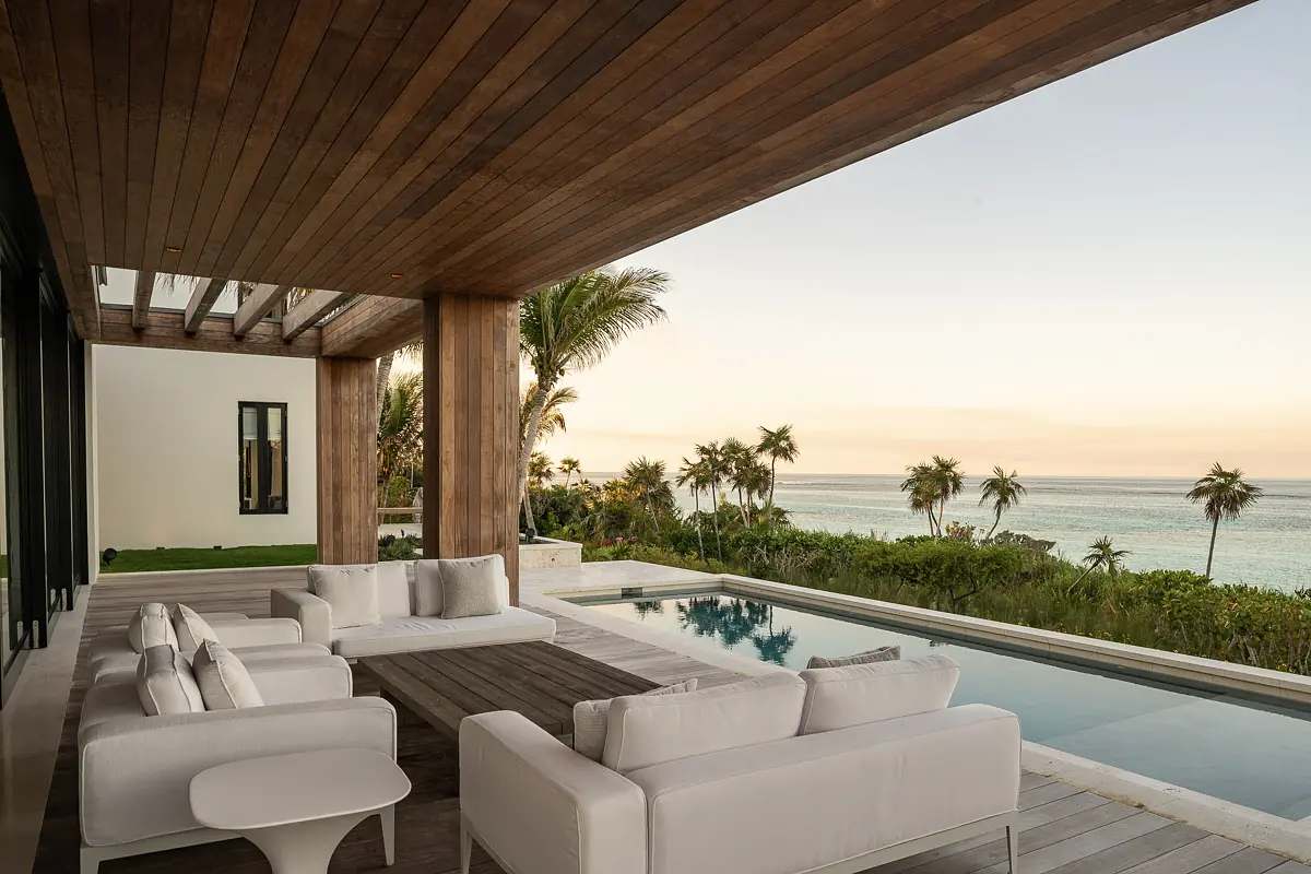 Deck with wooden ceiling, white outdoor sofa, coffee table, swimming pool, and ocean view