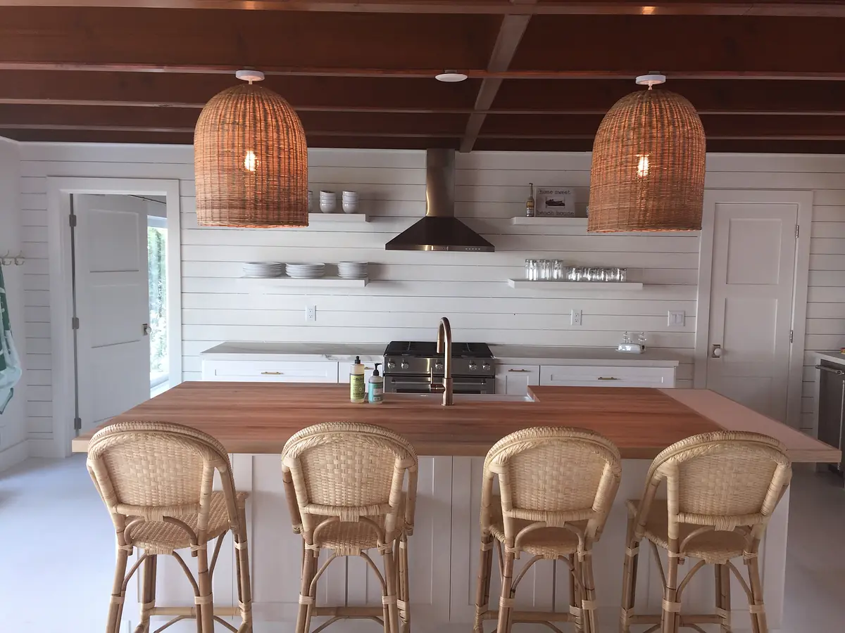 Kitchen with wooden island, rattan bar stools, stainless steel stove, and white shiplap walls