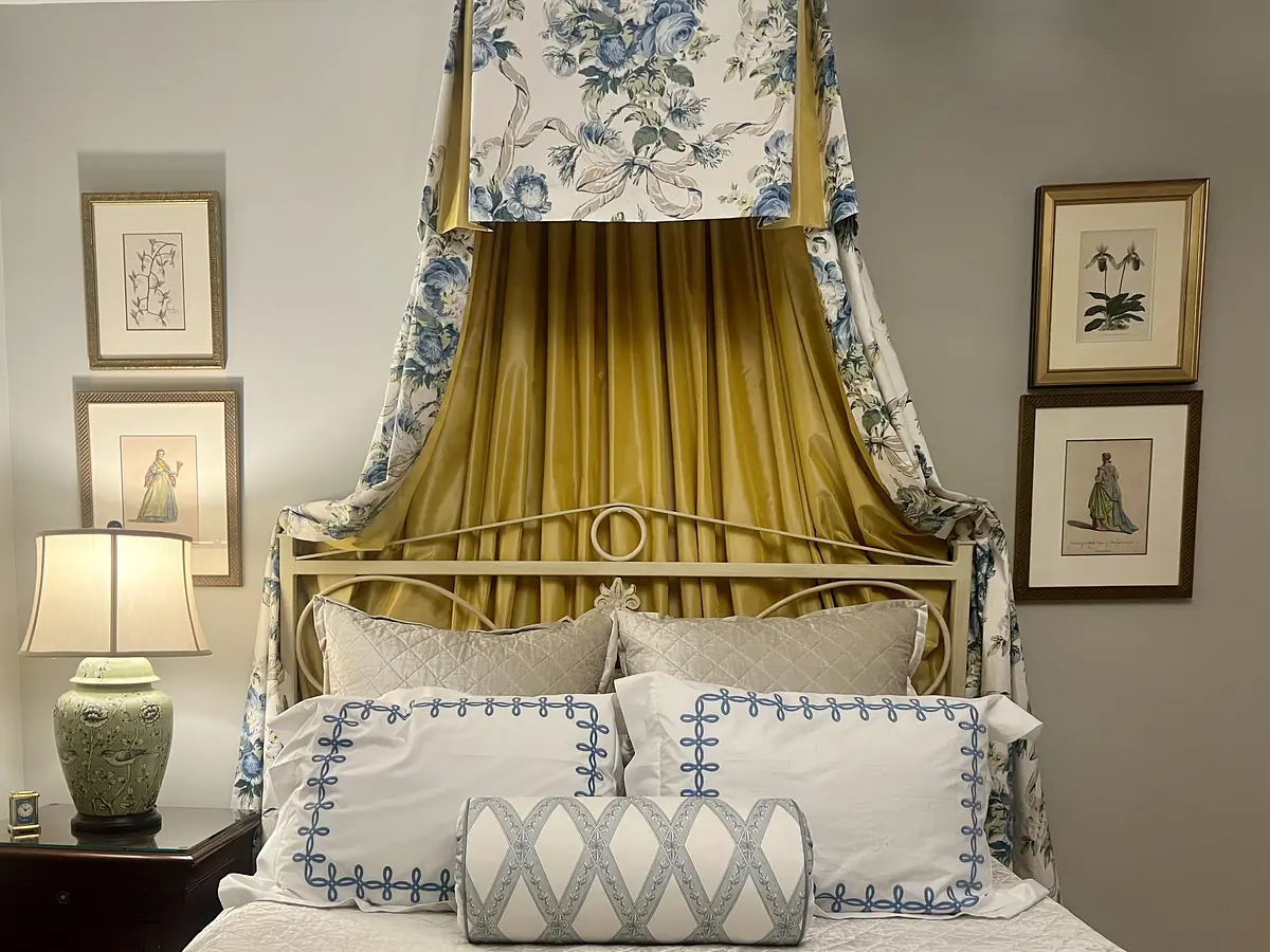 Bedroom with bed, yellow floral canopy, white bedding, decorative pillows, and framed artwork