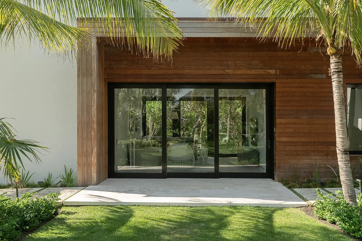 Exterior front with large sliding doors, wooden siding, palm trees, and a stone path.
