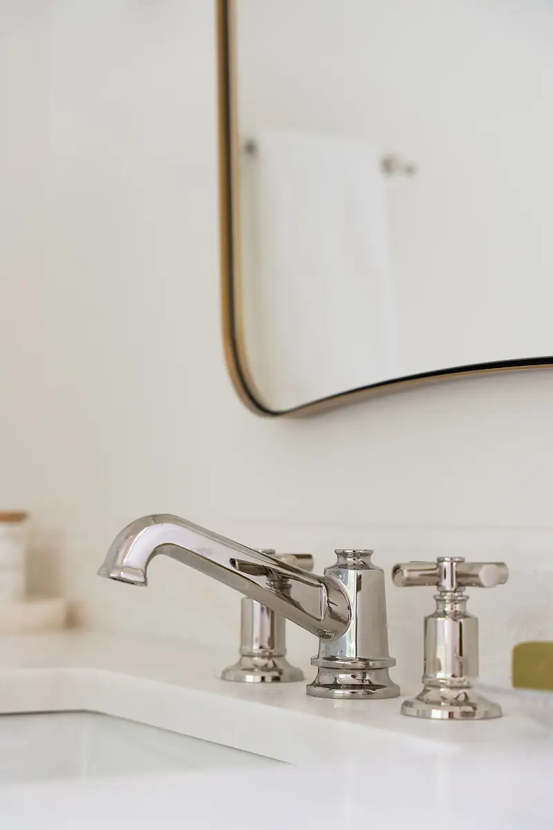 Bathroom sink area with chrome faucet, two handles, mirror, and white sink surface.