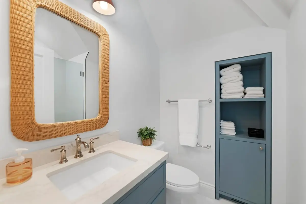 Bathroom with blue vanity, white countertop, sloped ceilings, towel rack, and storage unit.