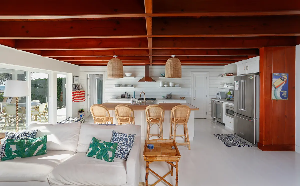 Kitchen with white island, bar stools, wood beams, shelving, and large windows for natural light.