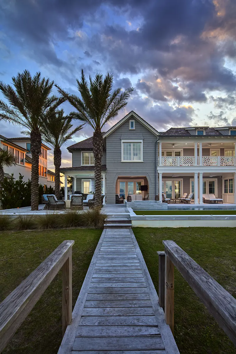 Exterior rear of a house with walkway, pool, palm trees, and gray facade.