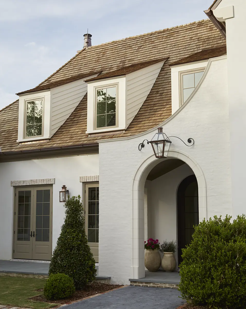 Exterior front of a house with peaked roof, white brick, arched entryway, planters, and lantern fixture.